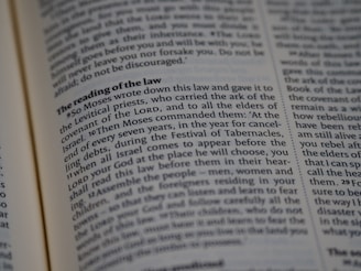 A close-up view of a page from a religious text, featuring printed paragraphs with a bold heading 'The reading of the law'. The text discusses instructions given by Moses about laws and the Festival of Tabernacles. The words are neatly aligned in columns.