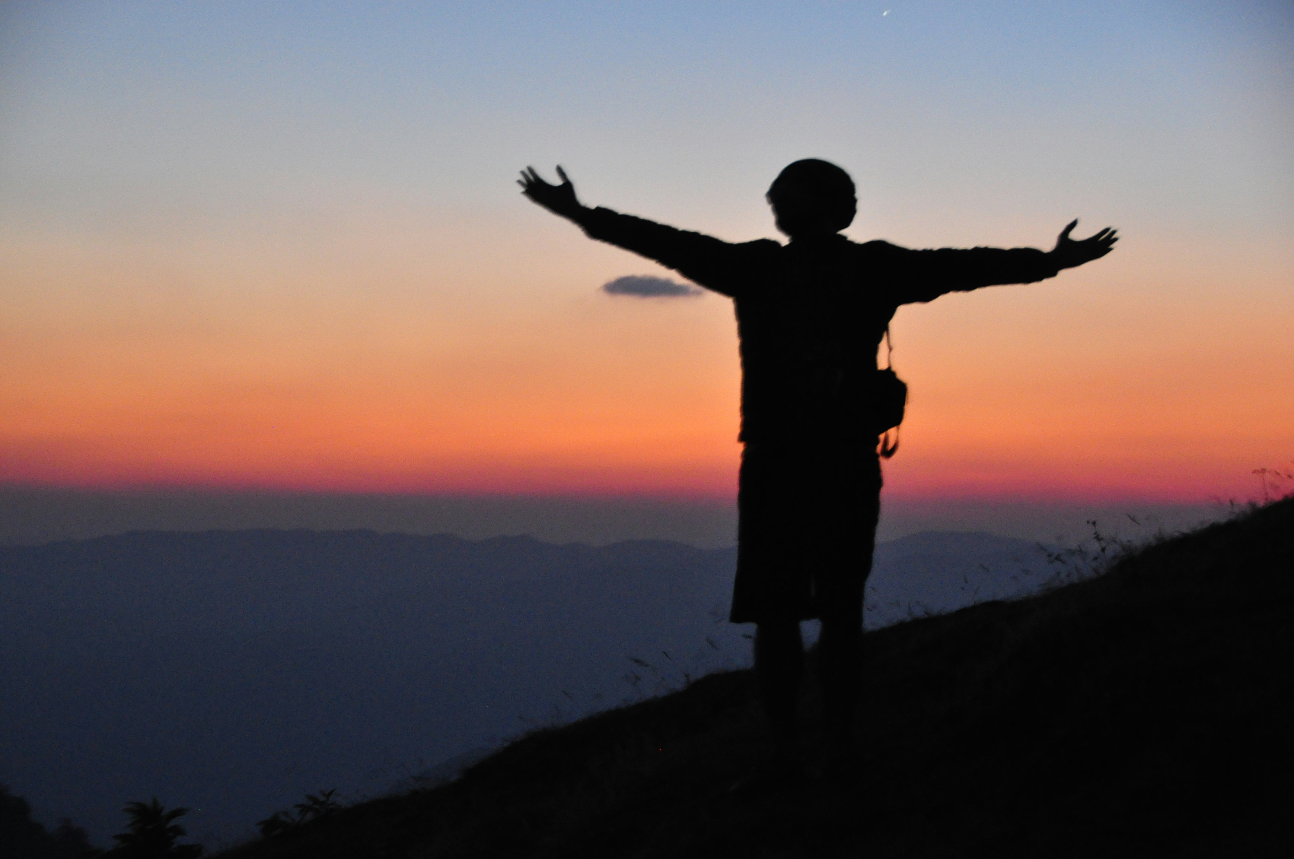 silhouette of man standing on hill during sunset
