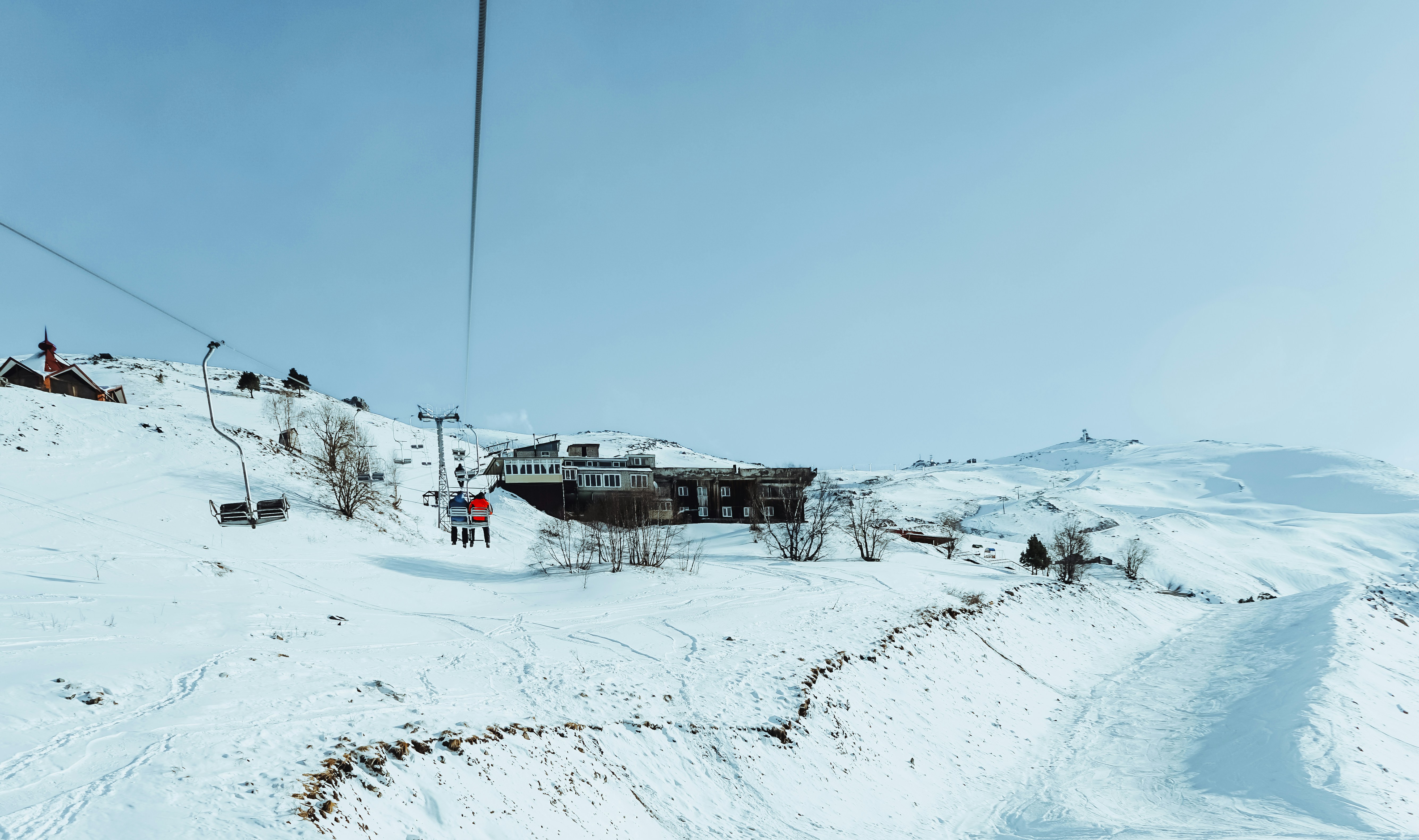 cable cars over snow covered ground during daytime, Two friends take a chair lift to the mountains in winter