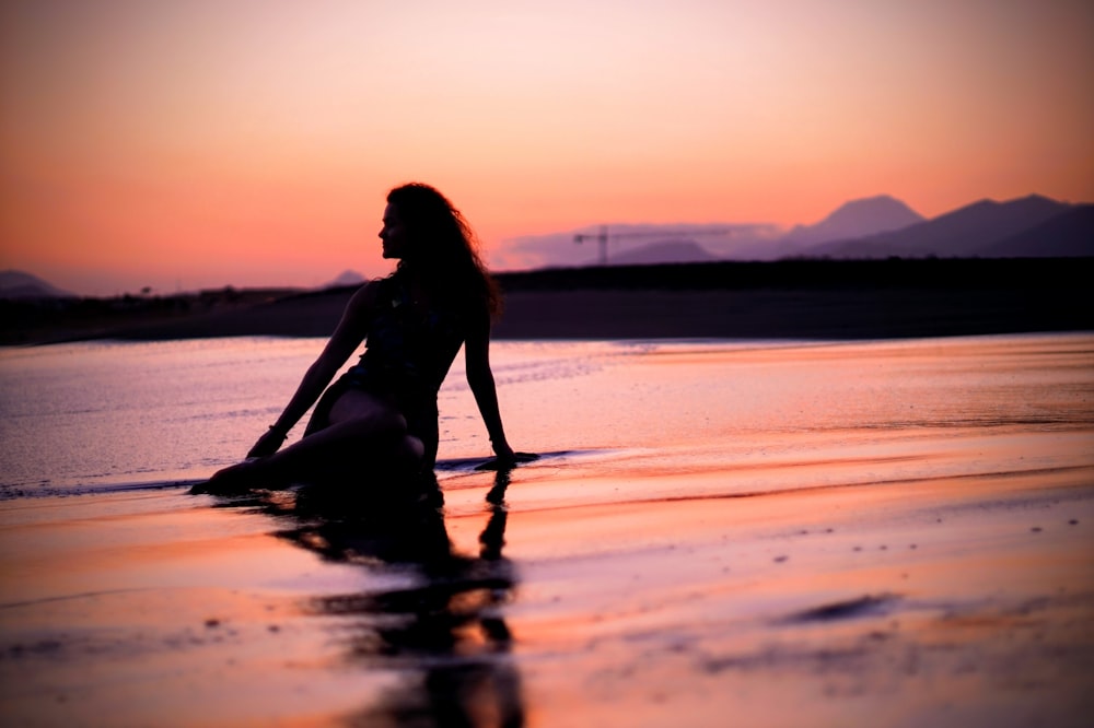 woman in black bikini sitting on beach during sunset