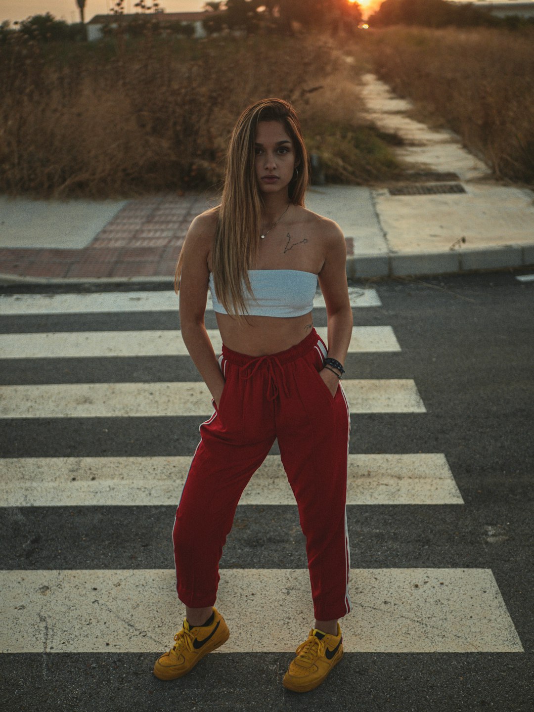 woman in white tank top and red pants standing on pedestrian line during daytime