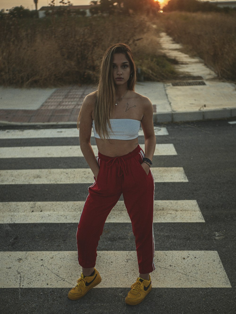 woman in white tank top and red pants standing on pedestrian line during daytime