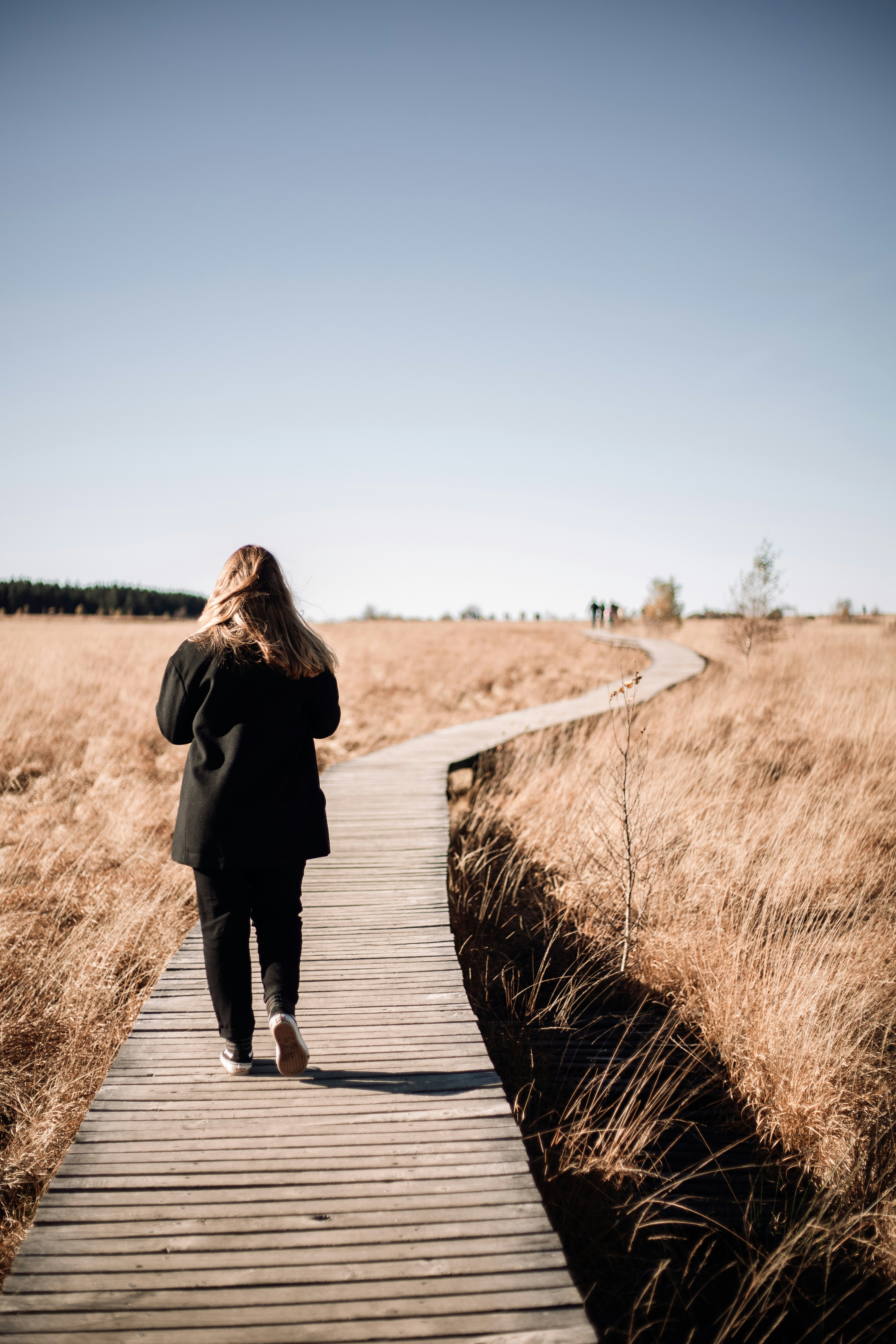 woman in black coat walking on brown wooden pathway during daytime