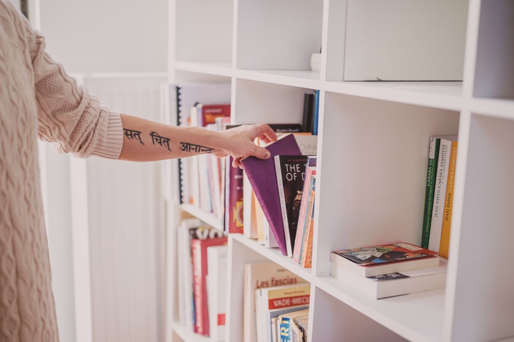 person holding books on white wooden shelf