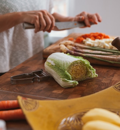 person slicing green vegetable on brown wooden chopping board