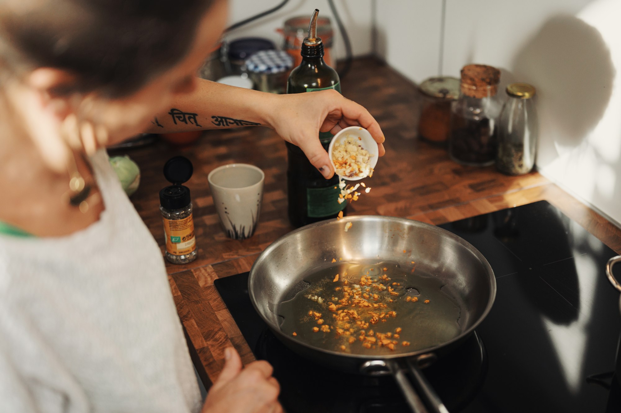 Woman adding herbs to heated oil in a sterling pan on a glass stove top.