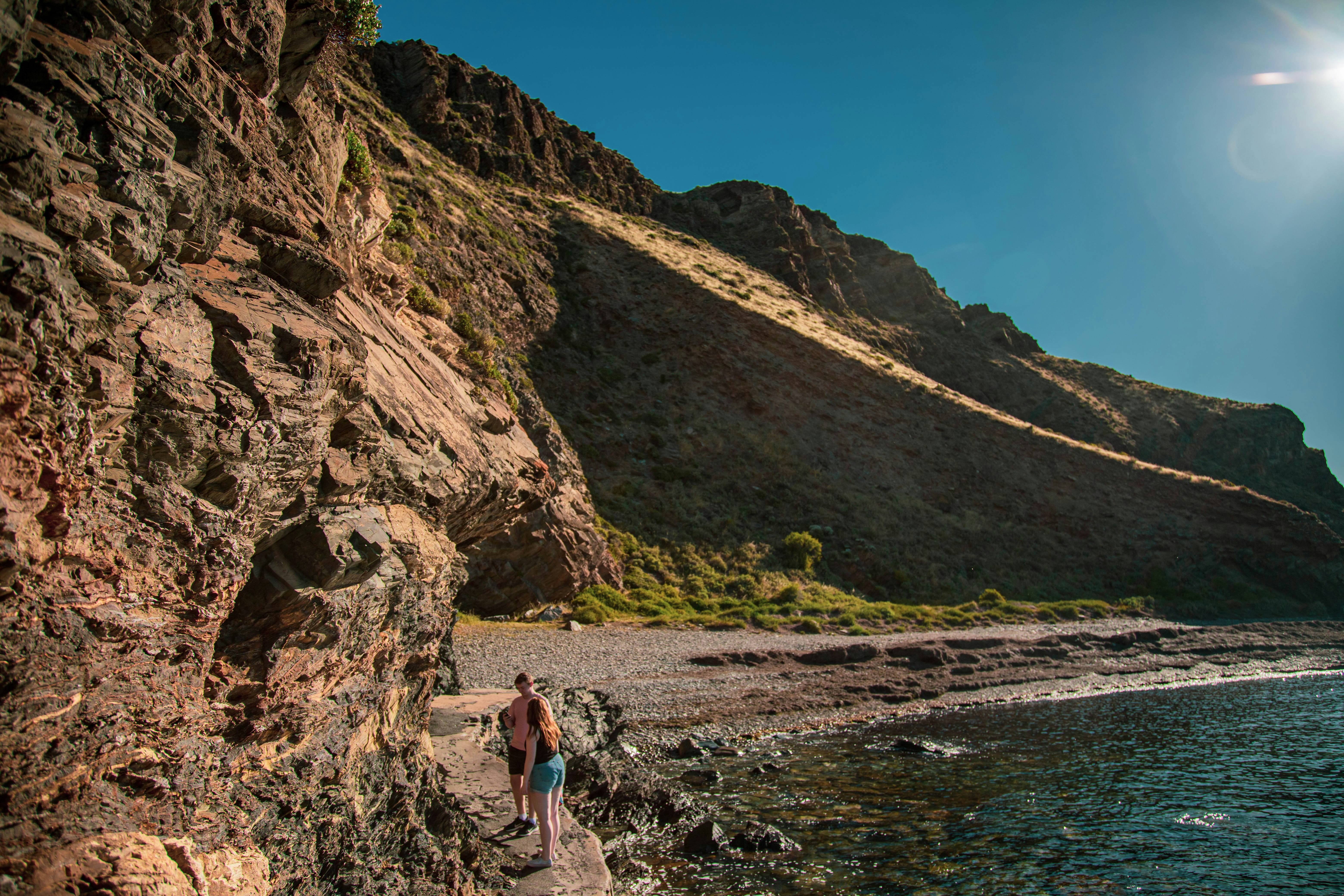 woman in blue tank top and blue denim shorts standing on rocky shore during daytime