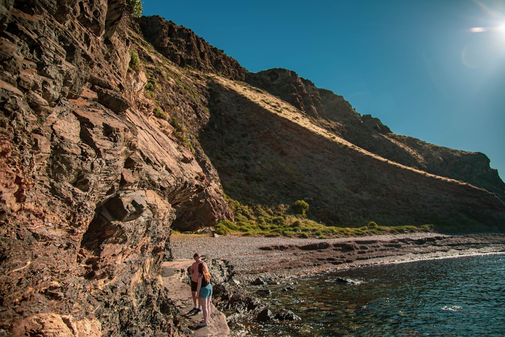 woman in blue tank top and blue denim shorts standing on rocky shore during daytime