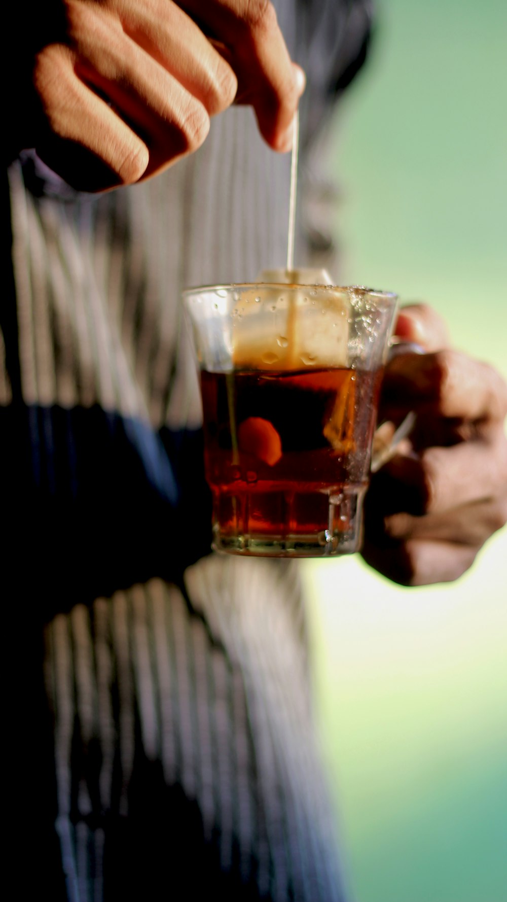 person holding clear shot glass with brown liquid