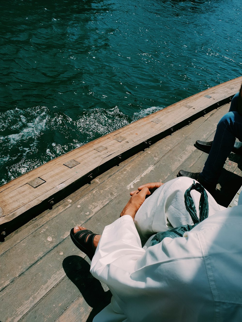 person in white shirt and black pants sitting on brown wooden dock