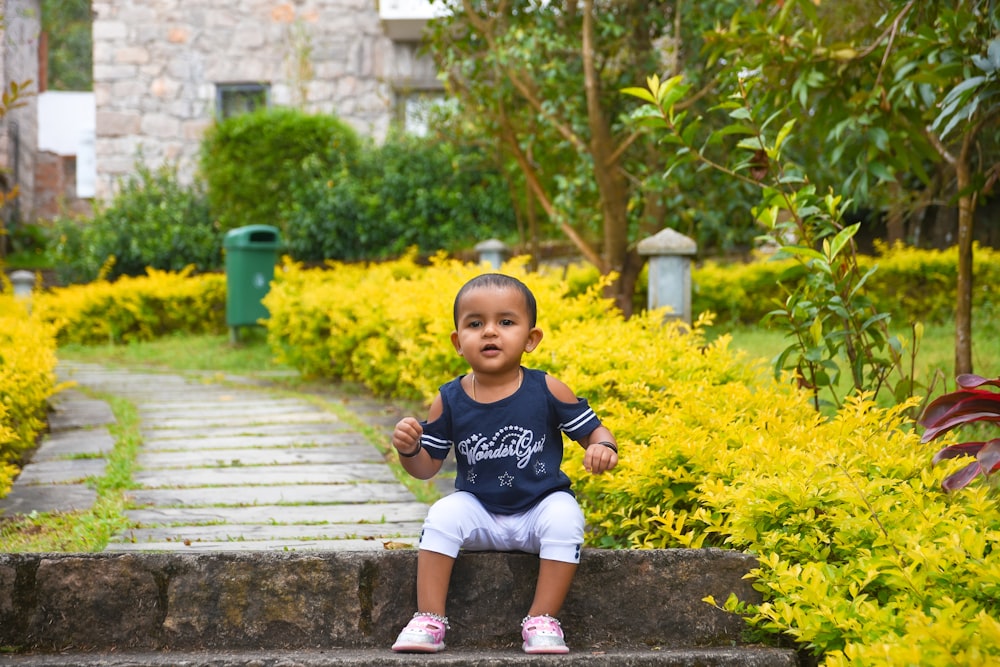 boy in blue crew neck t-shirt sitting on brown wooden stairs during daytime