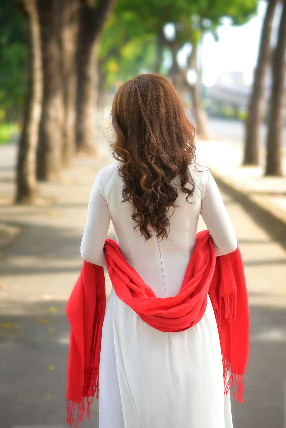 woman in white long sleeve shirt and red scarf standing on road during daytime