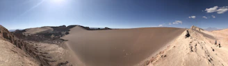A group of hikers pausing on a sunlit desert trail, surrounded by vast golden dunes under a clear blue sky.