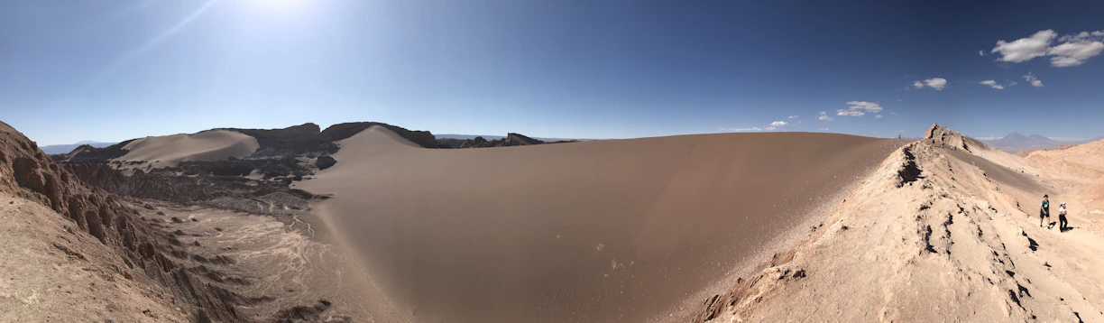 A group of hikers pausing on a sunlit desert trail, surrounded by vast golden dunes under a clear blue sky.
