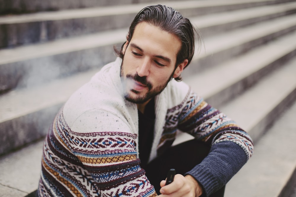 man in white sweater holding black smartphone