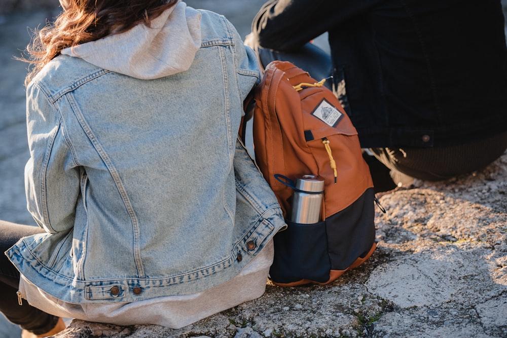 Mujer en chaqueta de mezclilla azul y mochila marrón de pie cerca de la mochila marrón