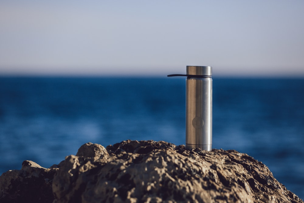 stainless steel tube on brown rock near blue sea during daytime