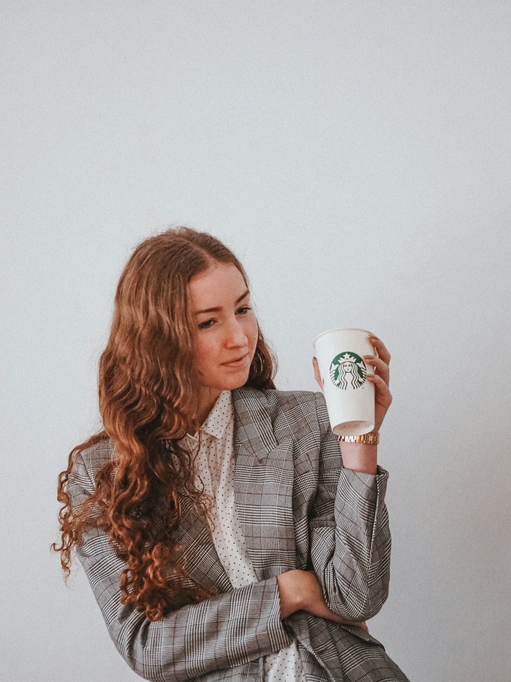 Femme en blazer gris tenant une tasse en céramique blanche