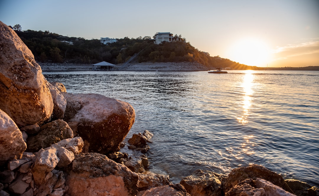 person in yellow jacket sitting on rock near body of water during daytime