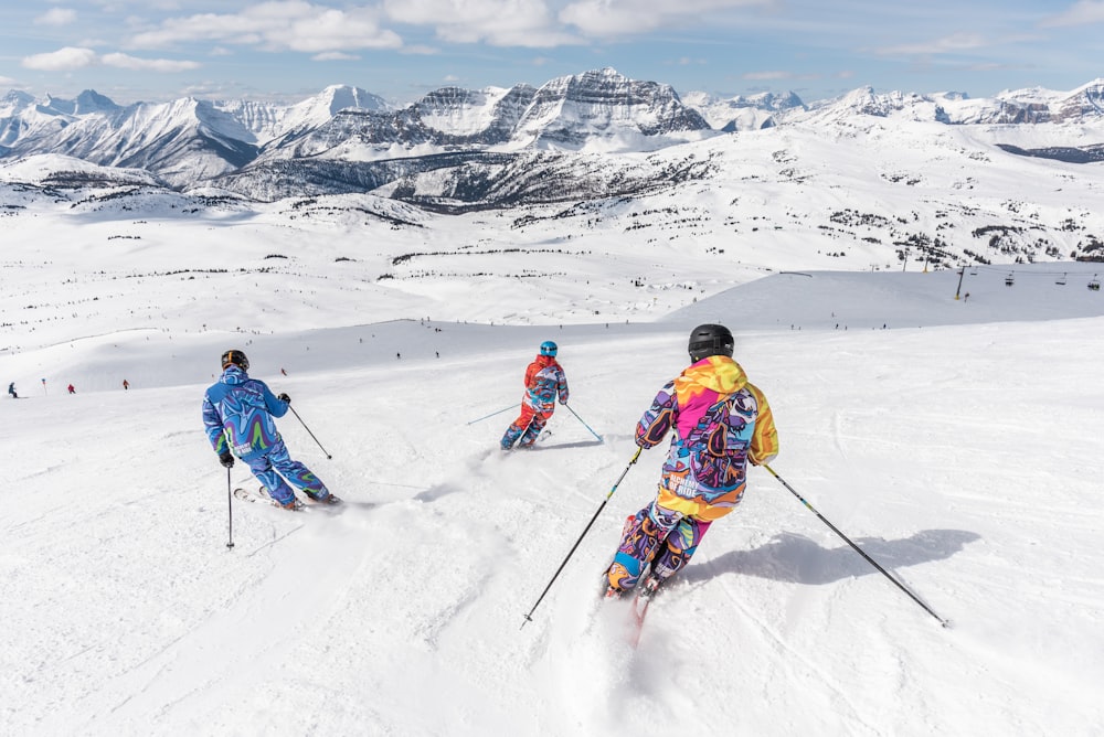 黄色いジャケットと青いヘルメットをかぶった2人が雪に覆われた山でスキーブレードに乗っています。
