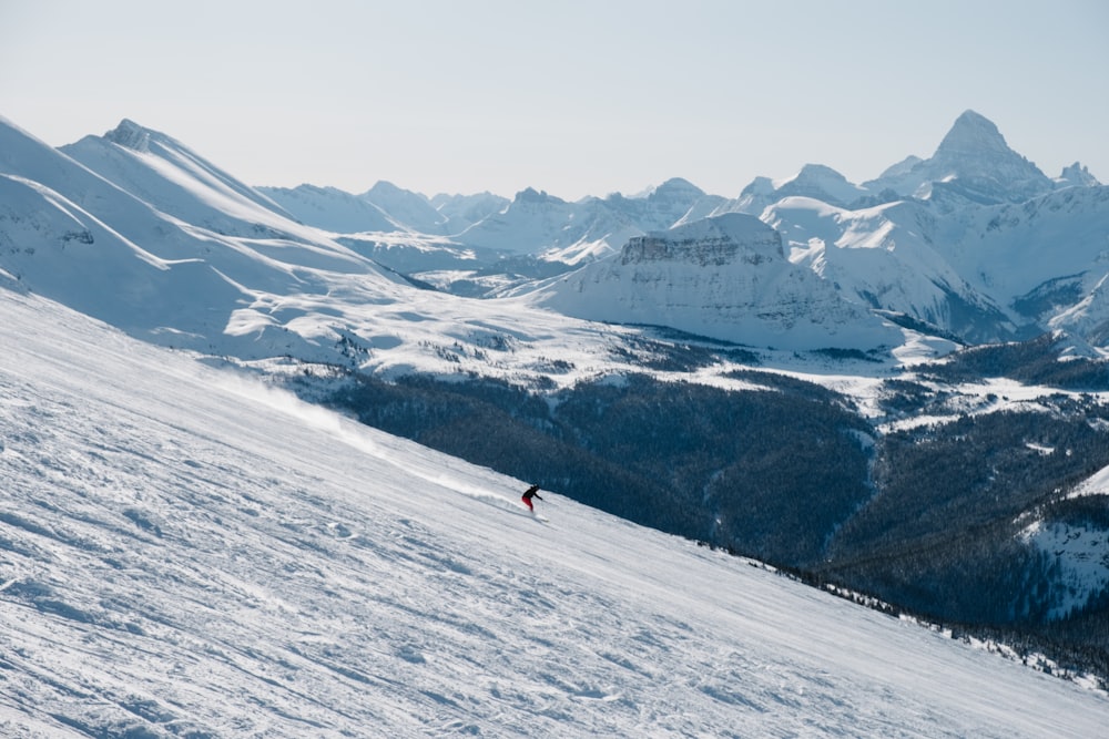 person in red jacket and black pants standing on snow covered mountain during daytime