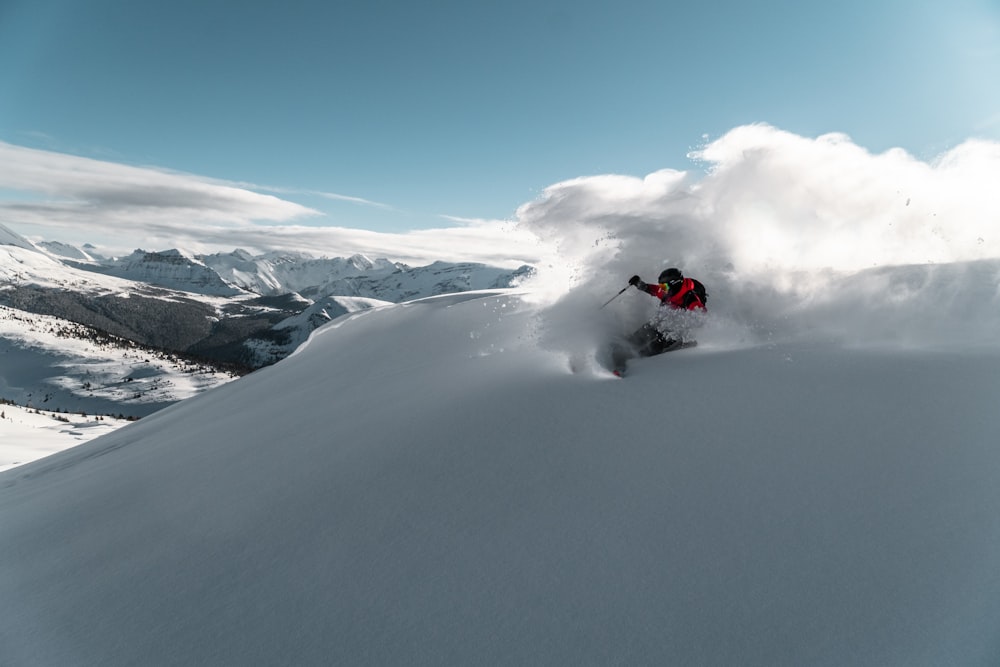 person riding red snow mobile on snow covered mountain during daytime