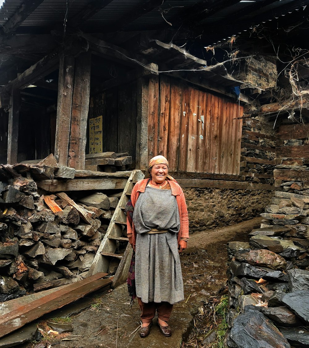 woman in brown and white dress standing near brown wooden house during daytime