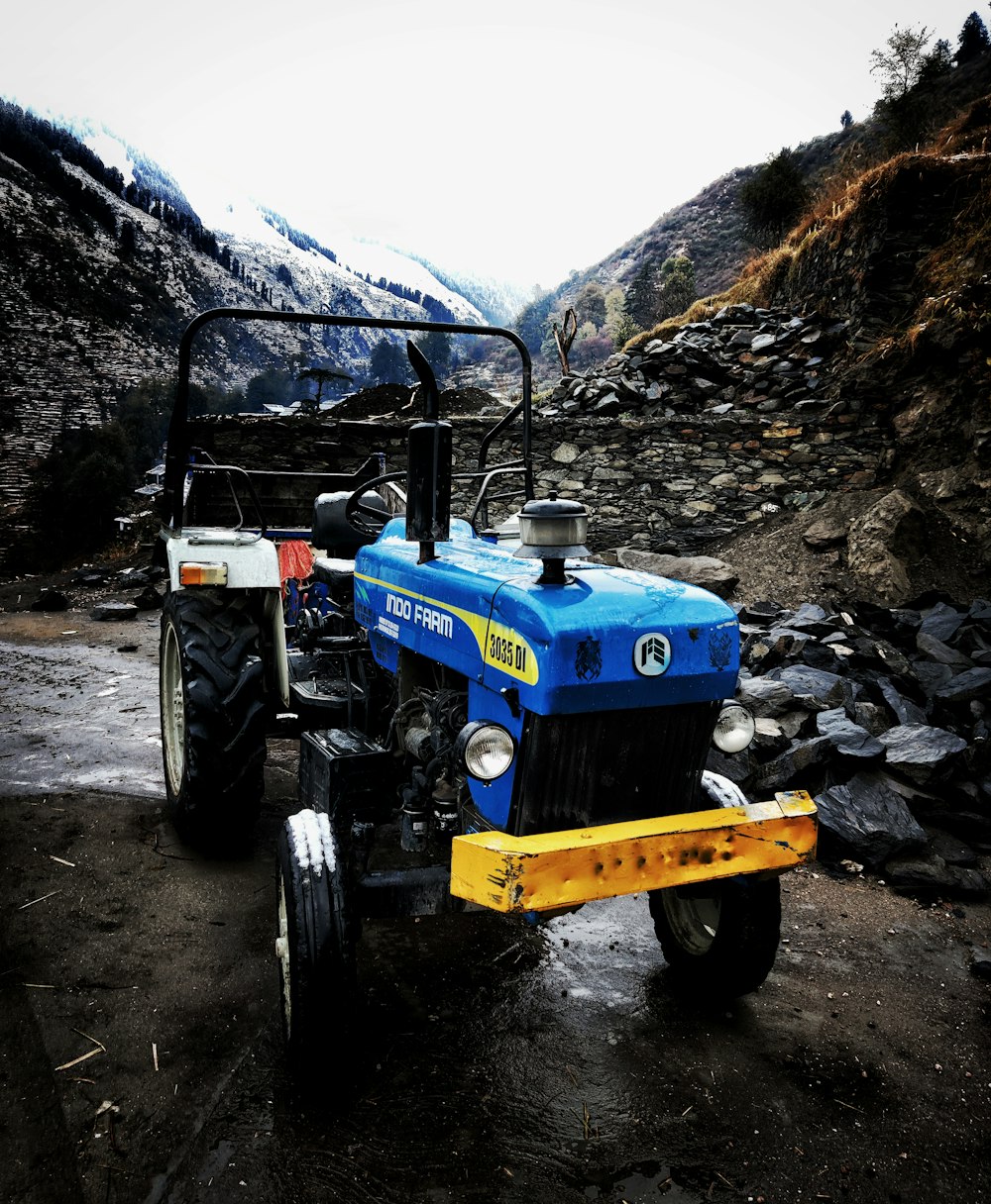 blue and yellow tractor on rocky ground near mountain during daytime