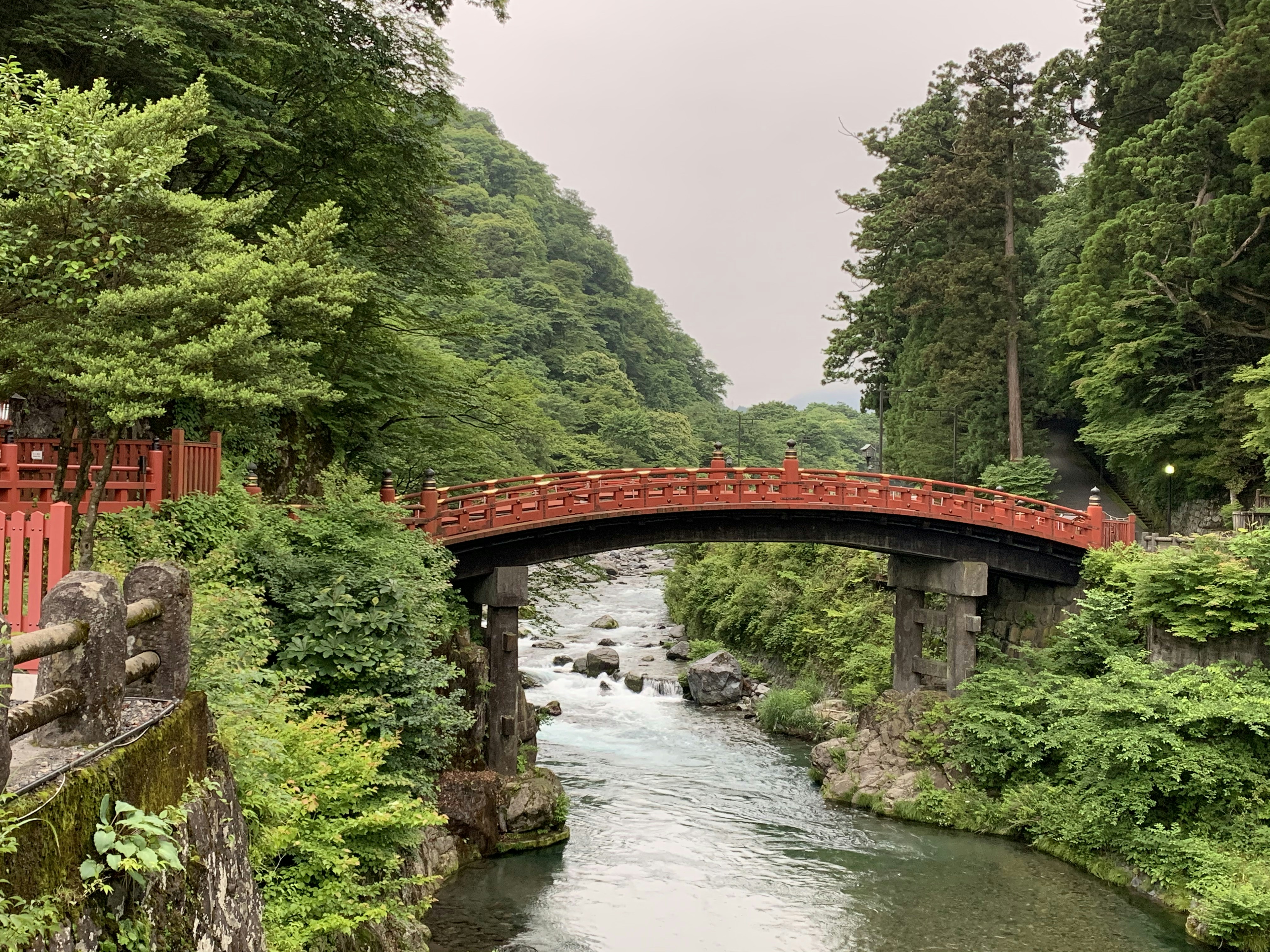 red bridge over river between green trees during daytime, A bridge between the montains