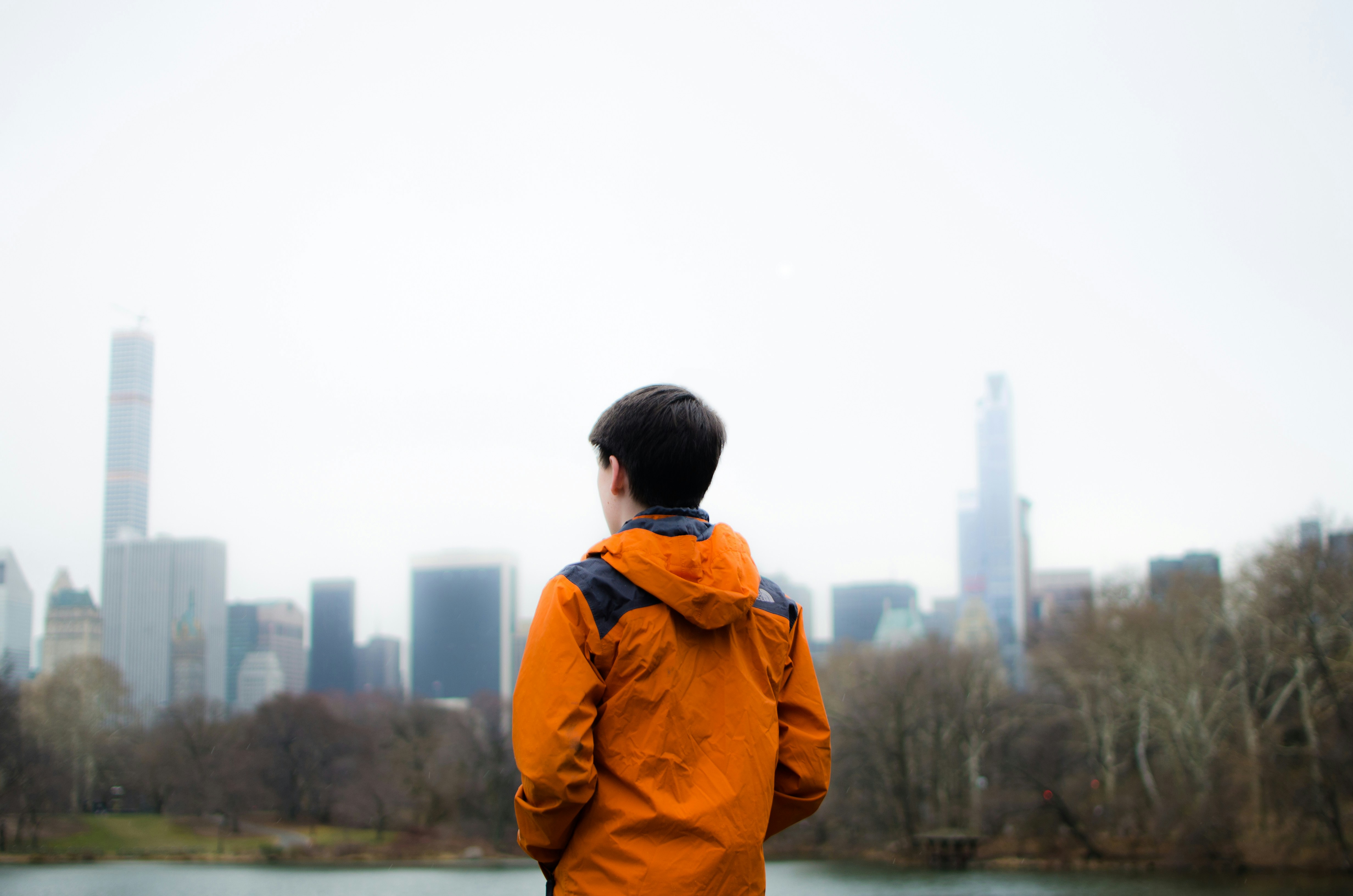 man in orange jacket standing near body of water during daytime