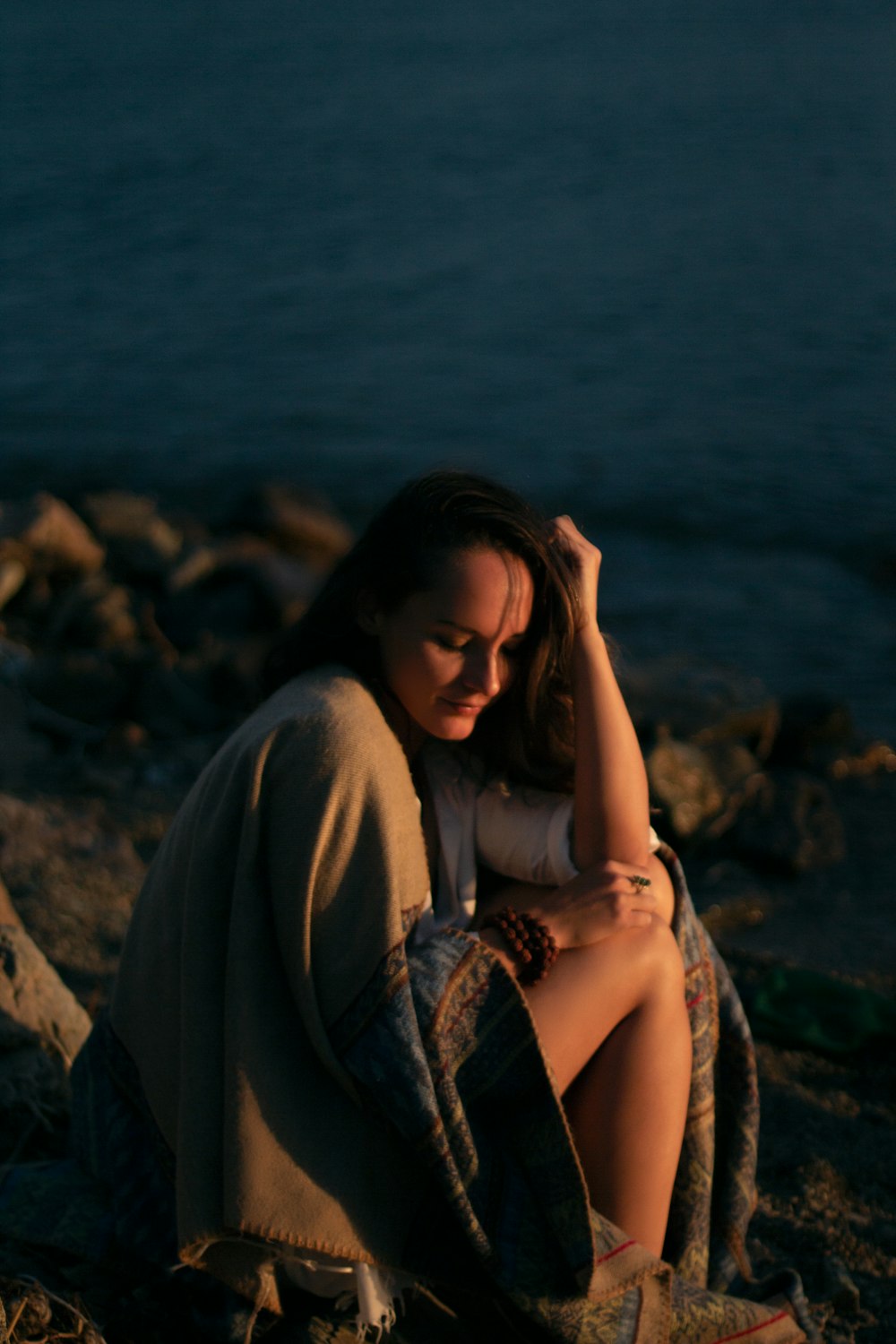 Mujer con camisa blanca sentada en la roca cerca del cuerpo de agua durante el día