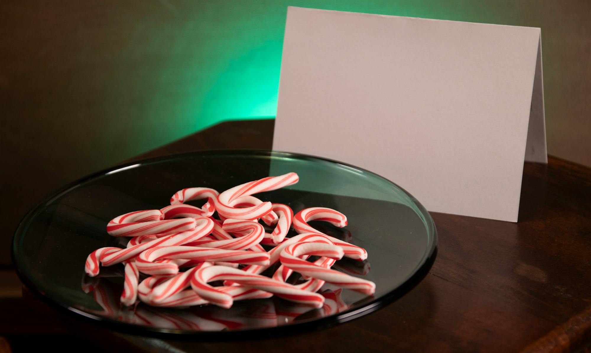 plate of candy canes on green plate with blank notecard and green spotlight backgroun