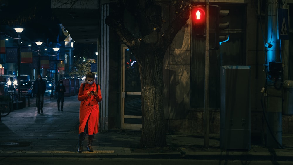 woman in red coat standing on sidewalk during night time