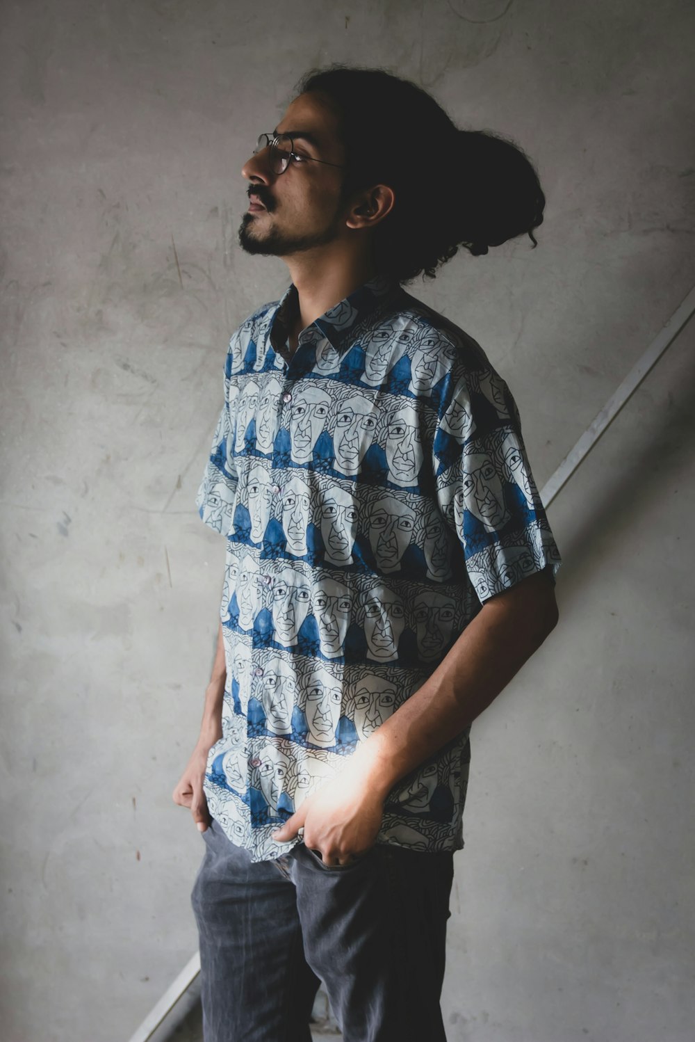 man in blue and white button up shirt standing beside white wall