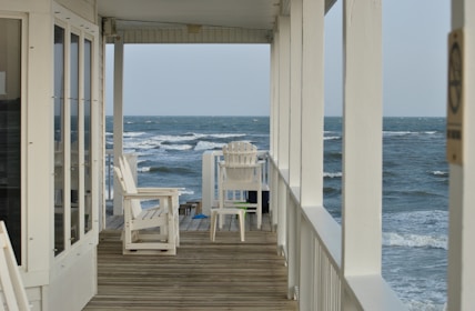 Charming beach house with a wooden deck, lounge chairs, and a view of the sparkling ocean at sunset.