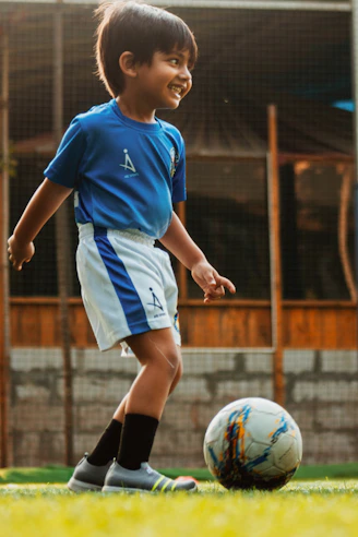 boy in blue and white soccer jersey kicking soccer ball