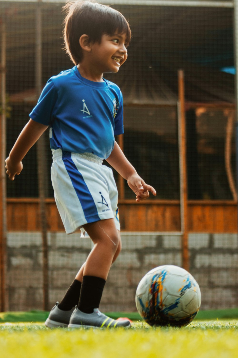 menino na camisa de futebol azul e branca chutando a bola de futebol