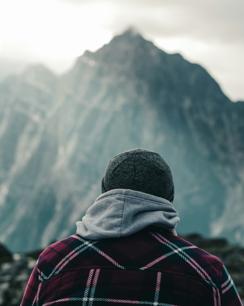 person in red and black jacket and gray knit cap looking at the mountains during daytime