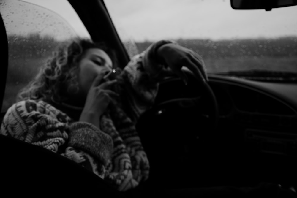grayscale photo of woman in jacket sitting inside car