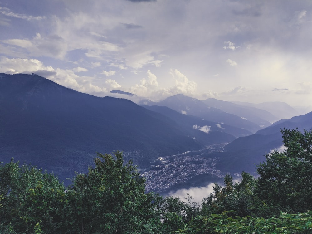 green trees and mountains under white clouds and blue sky during daytime