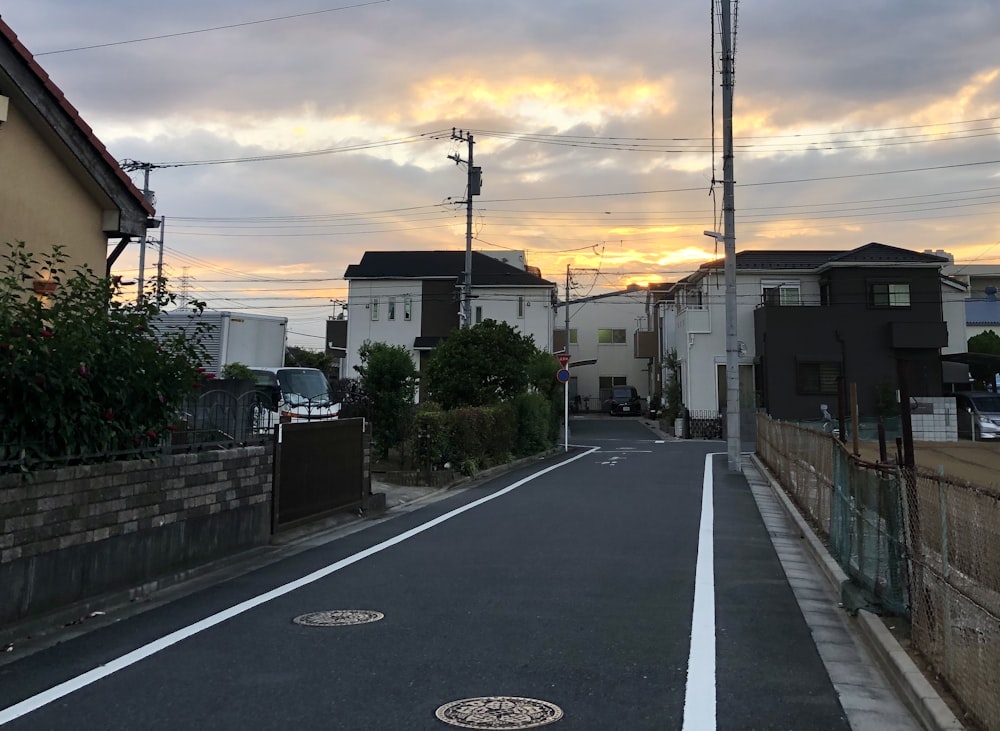 昼間は白い雲の下、灰色のアスファルト道路の脇に白と茶色のコンクリートの建物