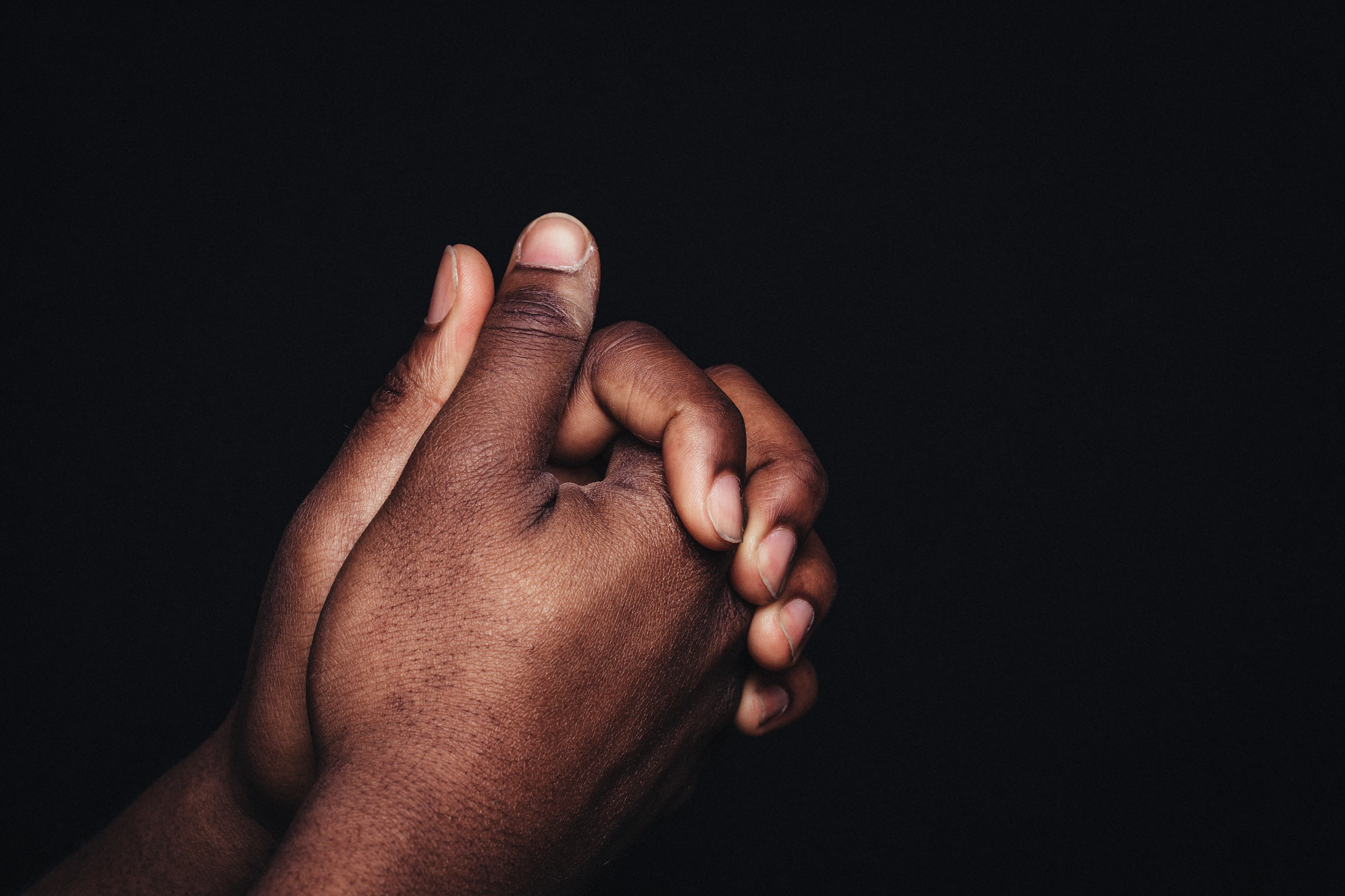 A hand reaching out to hold another in deep shadow