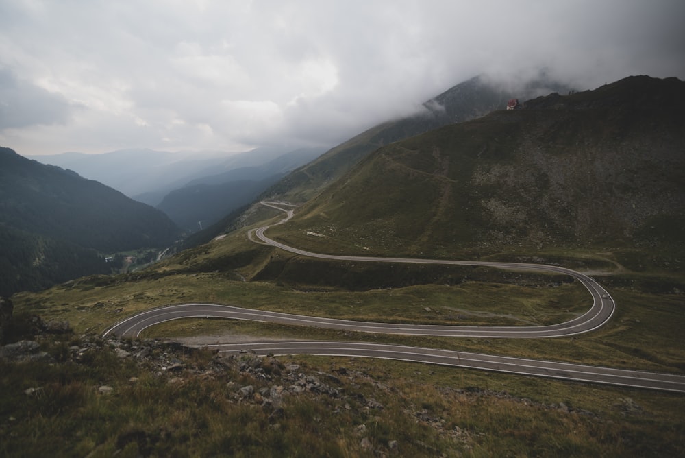 camino de asfalto gris entre montañas cubiertas de hierba verde bajo cielo nublado blanco durante el día