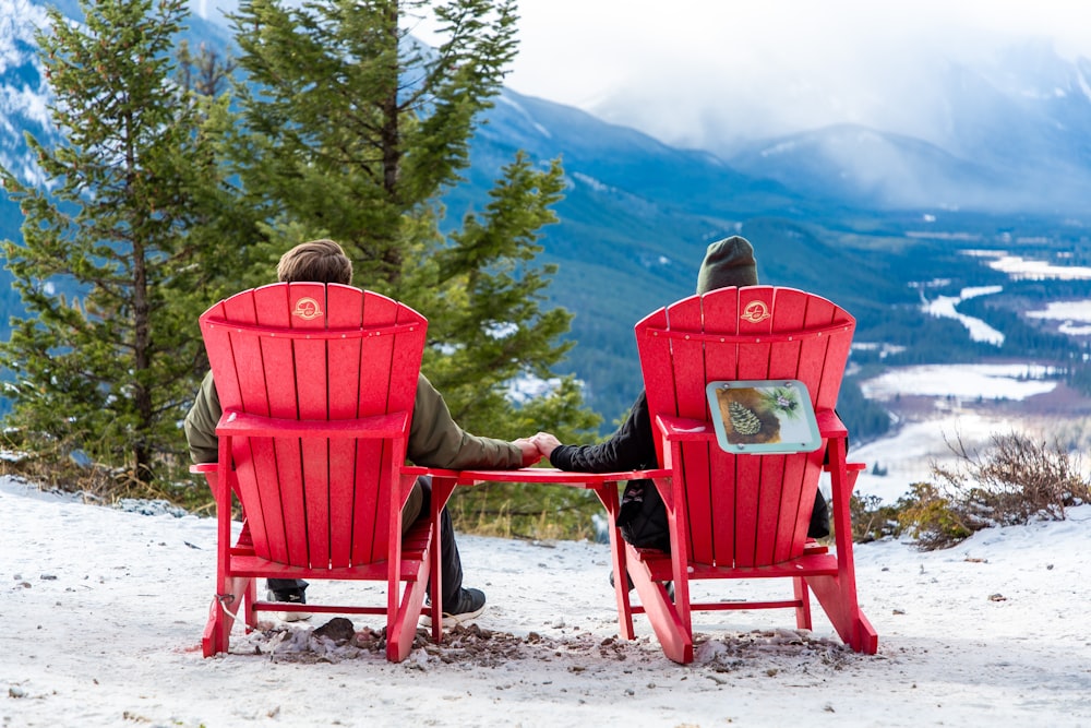 man in gray jacket sitting on red wooden armchair on white sand during daytime