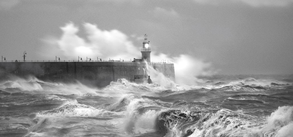 grayscale photo of sea waves crashing on concrete wall