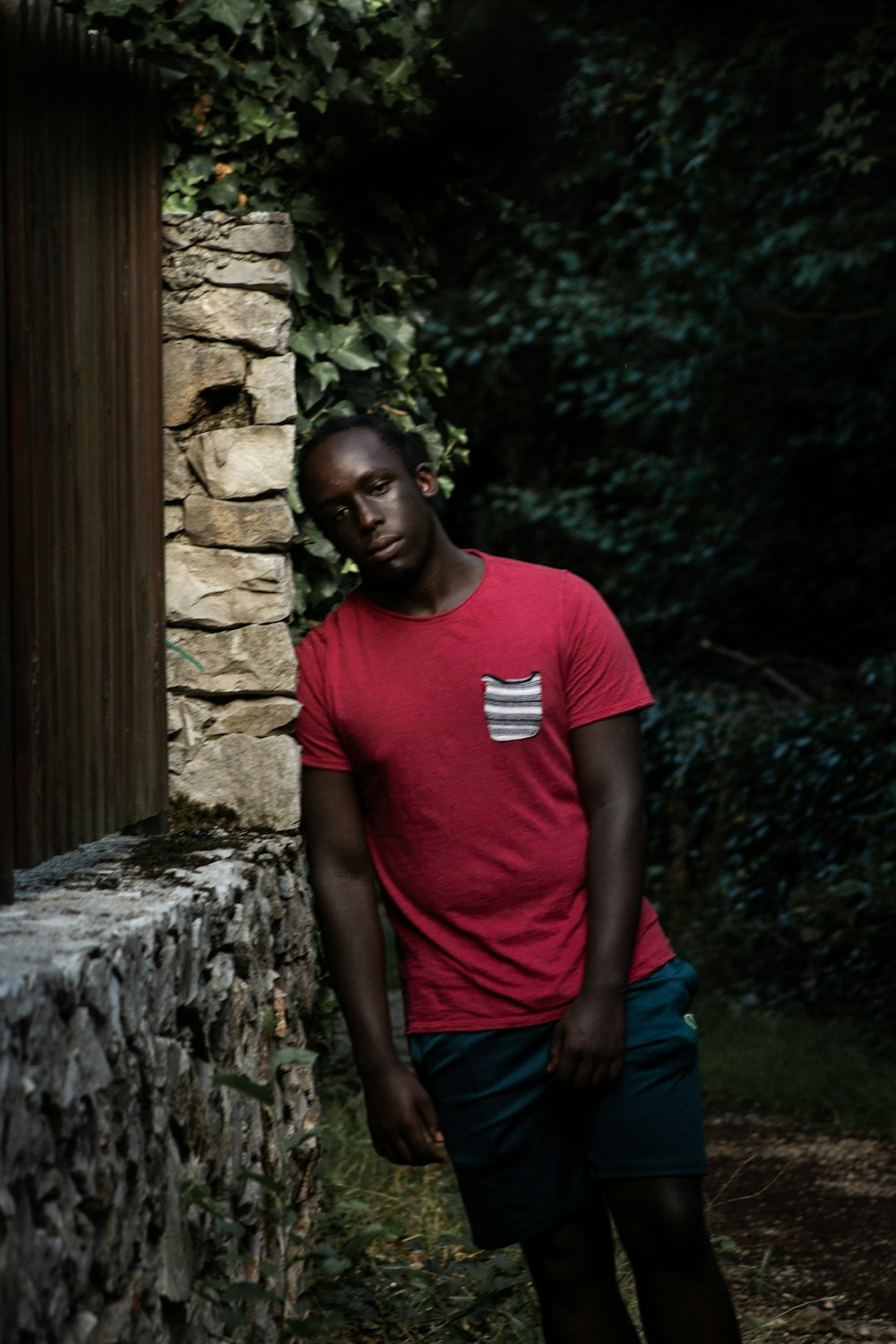 man in red crew neck t-shirt standing beside brown wooden door