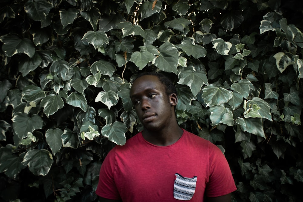 man in red crew neck t-shirt standing near green leaves