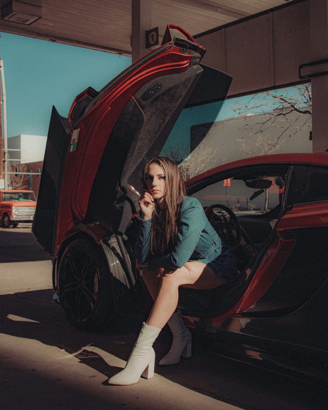 woman in blue long sleeve shirt and black pants leaning on red car