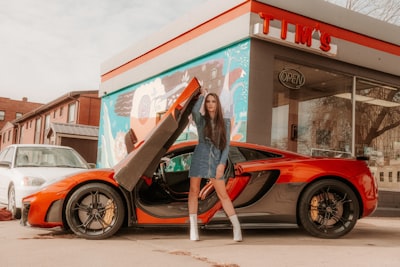 woman in blue denim jacket leaning on red car nebraska teams background