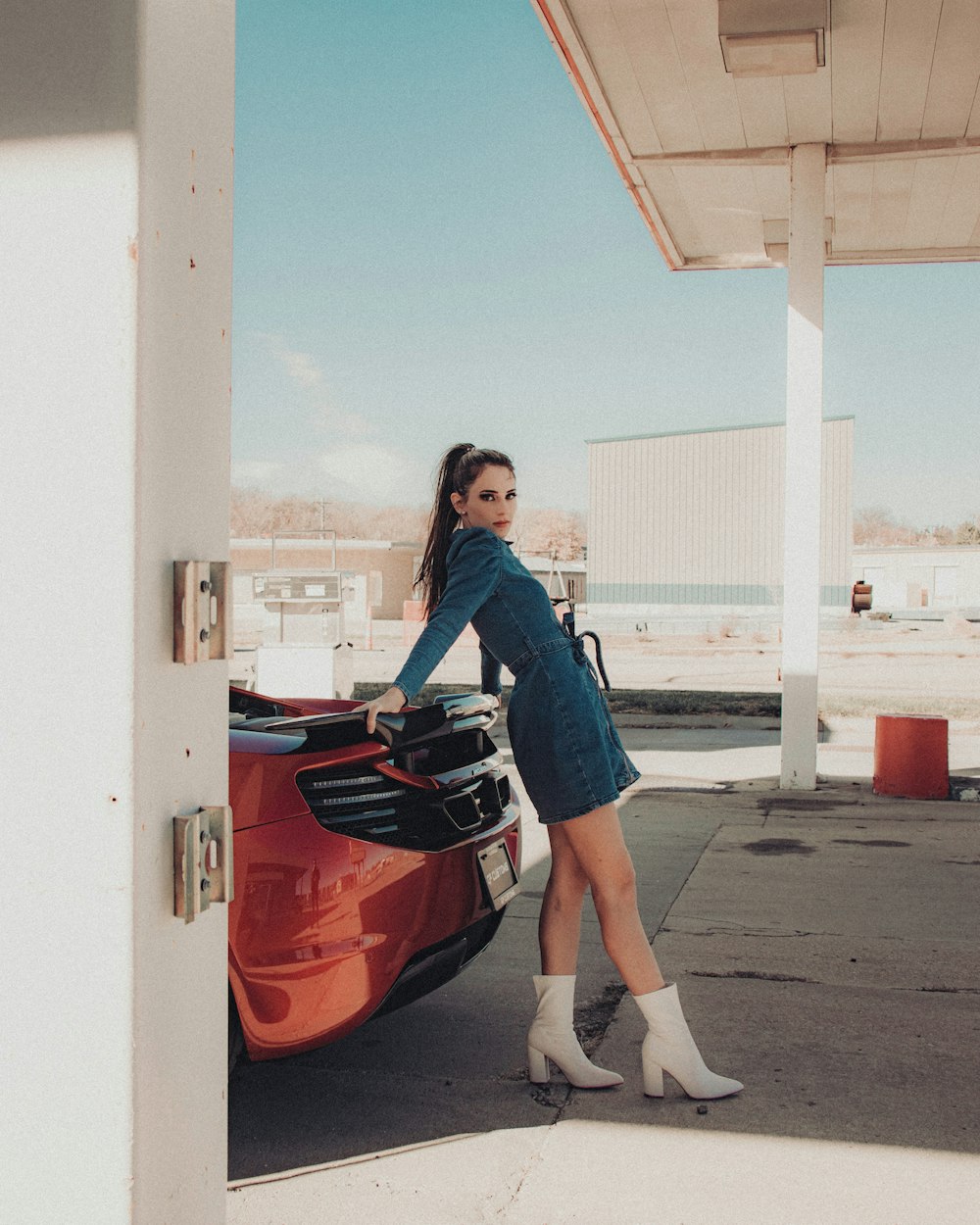 woman in blue and white plaid dress shirt and blue denim jeans standing beside red car